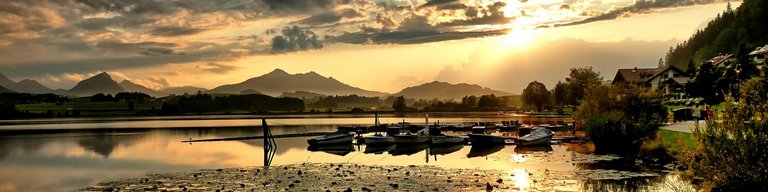 Sonnenuntergang am Hopfensee mit anliegenden Ruderbooten und vielen Seerosen im Vordergund